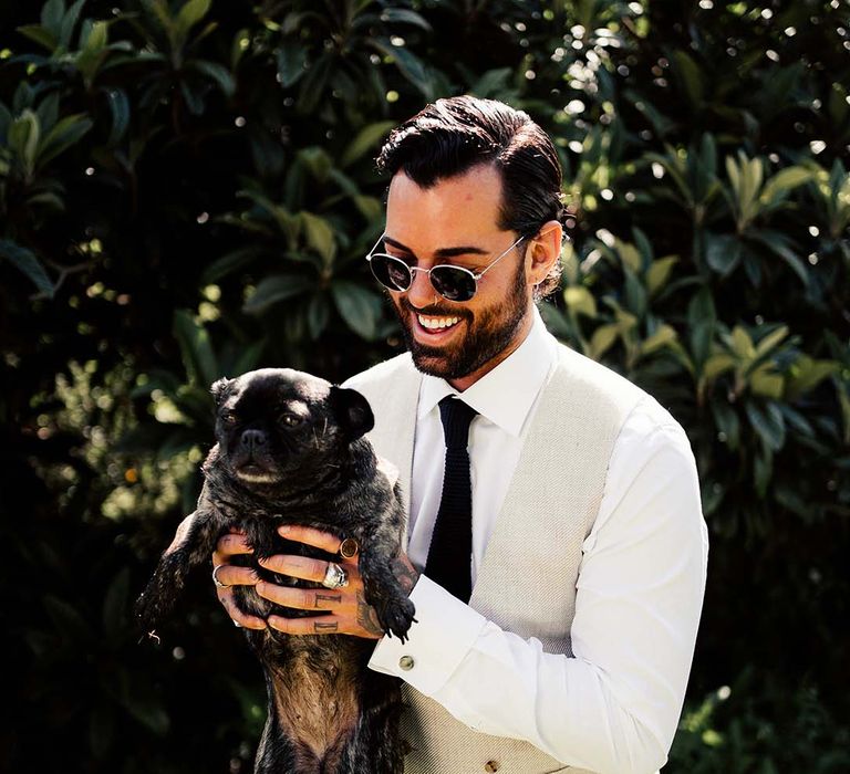 Groom in cream suit with dog at wedding