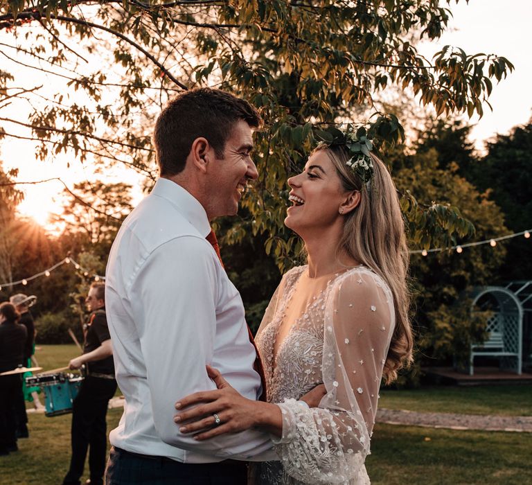 Bride in long sleeve embroidered Julie Vino wedding dress and boho flower crown dances with groom in white shirt during golden hour at wedding reception