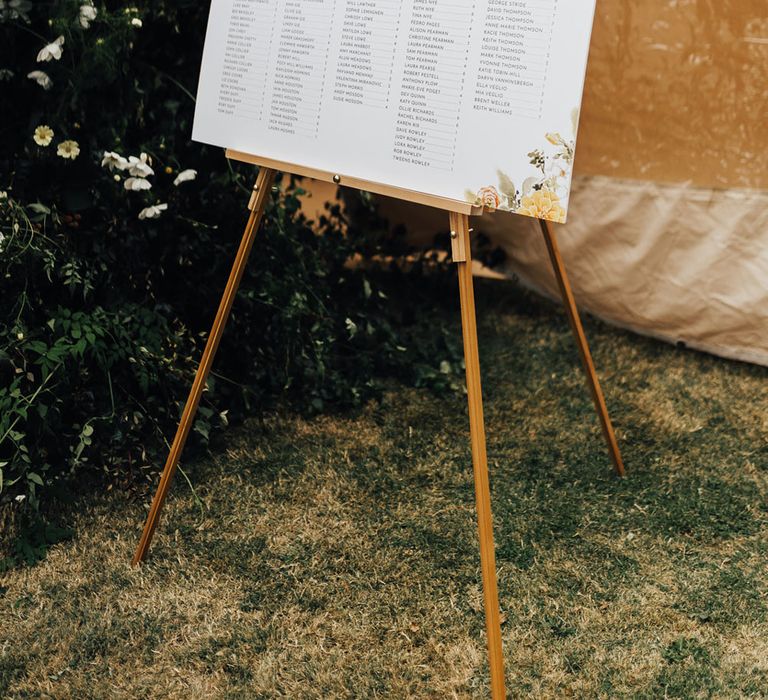 White wedding table plan on wooden easel with floral illustrations for sperry tent wedding reception