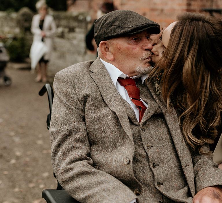 Female wedding guest in a brown satin dress kissing a male guest in a beige wool suit and flat cap