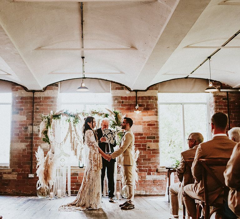 Bride & groom hold hands and look at one another on the day of their wedding during ceremony