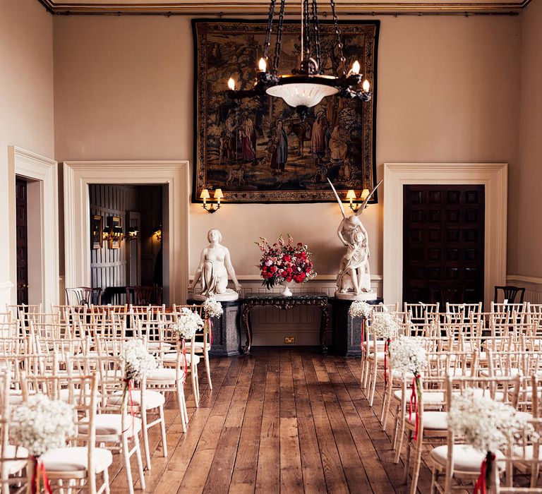 Interior of Elmore Court wedding ceremony room with white bamboo chairs, red wedding flowers and white classical statues on pedastals 