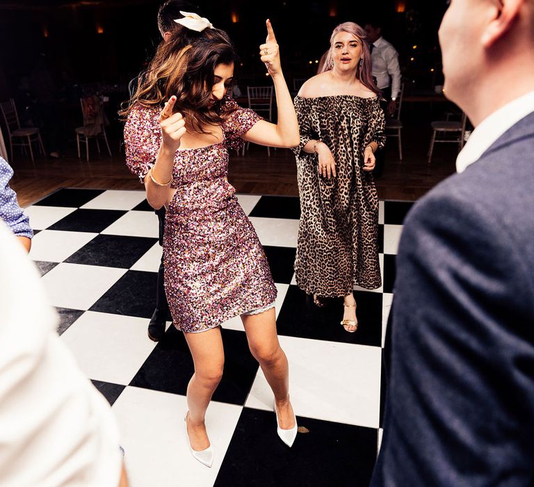 Bride in short pink glitter dress, white heels and hair bow dances on black and white dance floor at Elmore Court