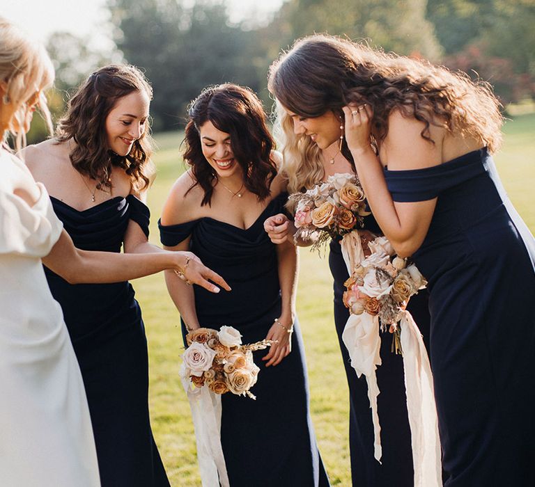 Bridesmaids in 1930s style navy blue dresses take a closer look at the bride's wedding rings