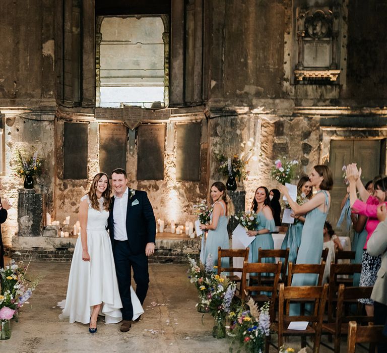 Guests applaud as bride and groom walk back down the aisle together as a married couple