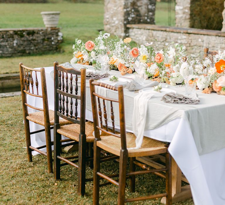 wooden table and chairs with white tablecloth and peach and coral floral centrepiece flowers 