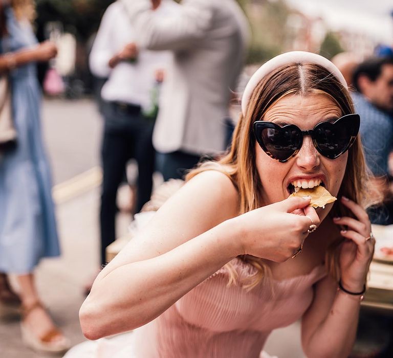 Bride in a blush pink wedding dress each nachos wearing black heart shaped sunglasses 