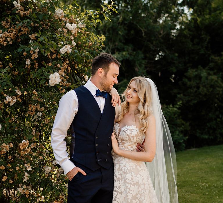 Bride in strapless wedding dress with veil with groom in dark blue waistcoat and bow tie