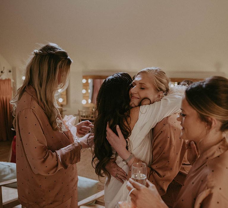 Bride hugs her bridesmaids as they all get ready for the wedding together 