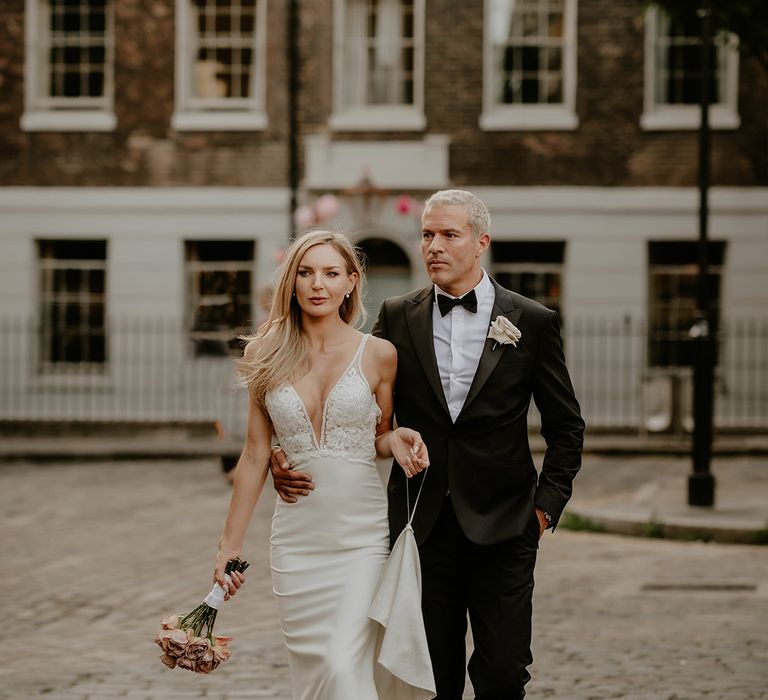 Bride in embellished wedding dress walking with the groom who rests his hand on her waist for city wedding 