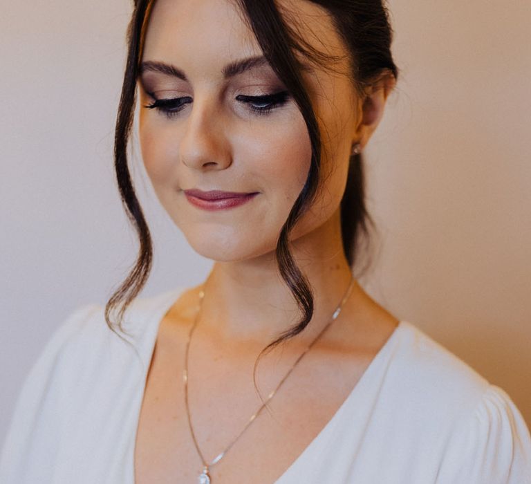 Bride with a subtle smoky eye makeup and ponytail wedding hair with a simple silver necklace 