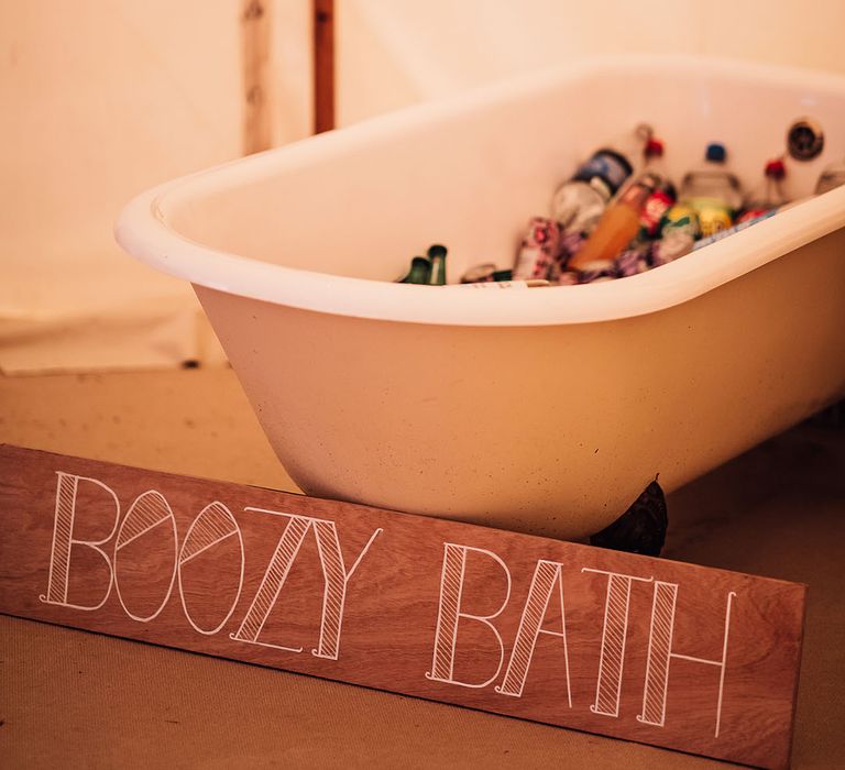 Old bath tub filled with alcoholic drinks and mixers with a wooden sign 