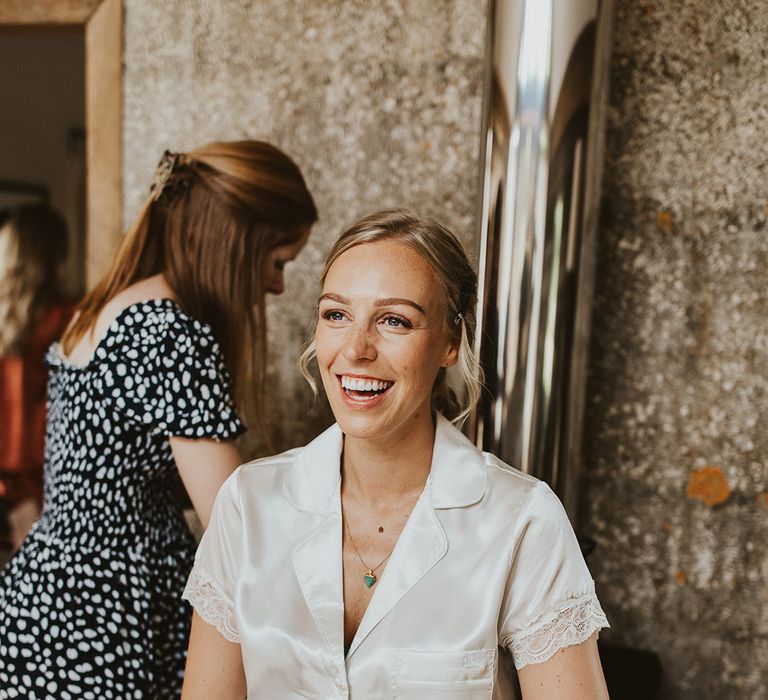 Bride smiles wearing white satin pyjamas with lace cuff detail as she gets ready for her wedding day 