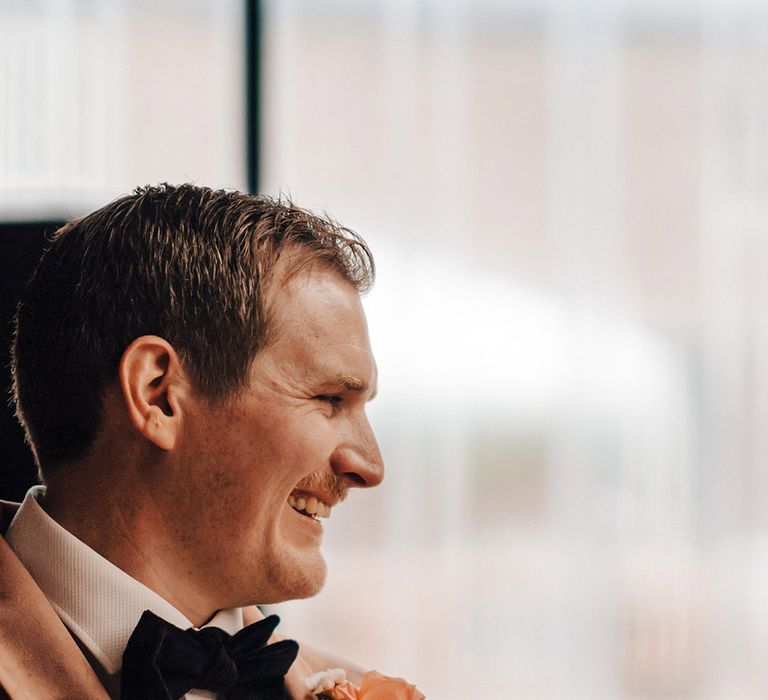 The groom wears a pale pink velvet suit jacket with a rose buttonhole 