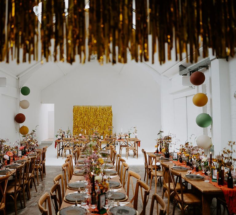 Wooden banquet tables with small floral arrangements and orange fabric table runners