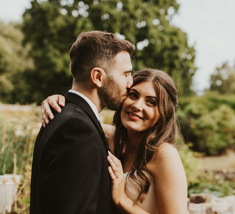 Groom in a morning suit kisses the bride on the forehead who wears a strapless Phillipa Lepley wedding dress 