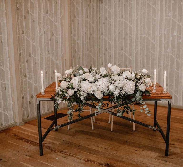 White roses and eucalyptus on wooden table complete with white candles