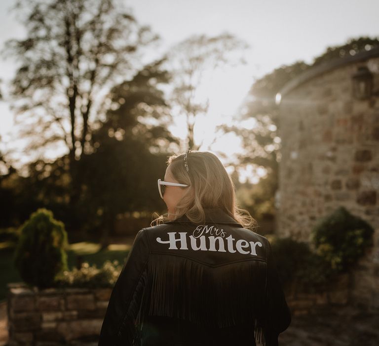 Bride in white heart shaped sunglasses, bridal tiara and personalised handmade black leather jacket with "Mrs Hunter" written on it