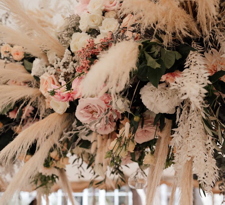 Pink and white wedding flower installation with pampas grass decor and hanging candles 