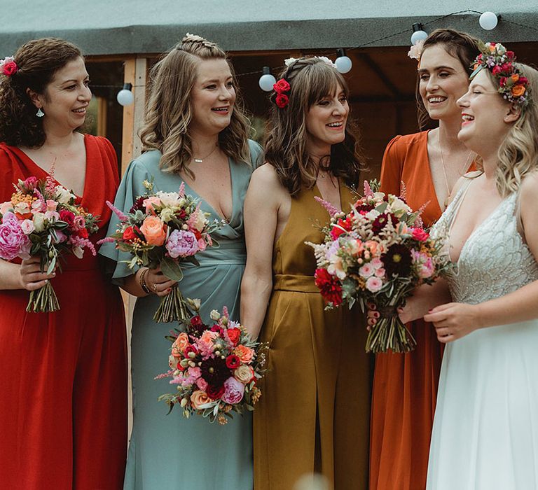 Bridesmaids in mismatched colourful dresses with the bride with flowers in their hair for festival tipi wedding 