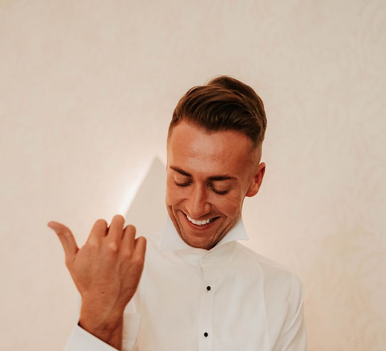 Groom fastening wedding cufflinks on crisp white shirt with black button details 