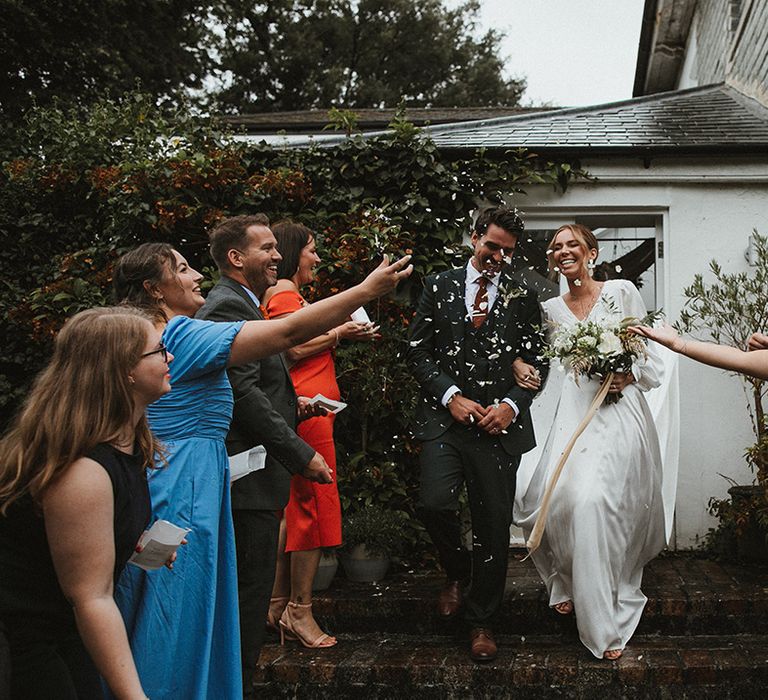 Bride & groom walk through white confetti during confetti exit after intimate wedding ceremony 