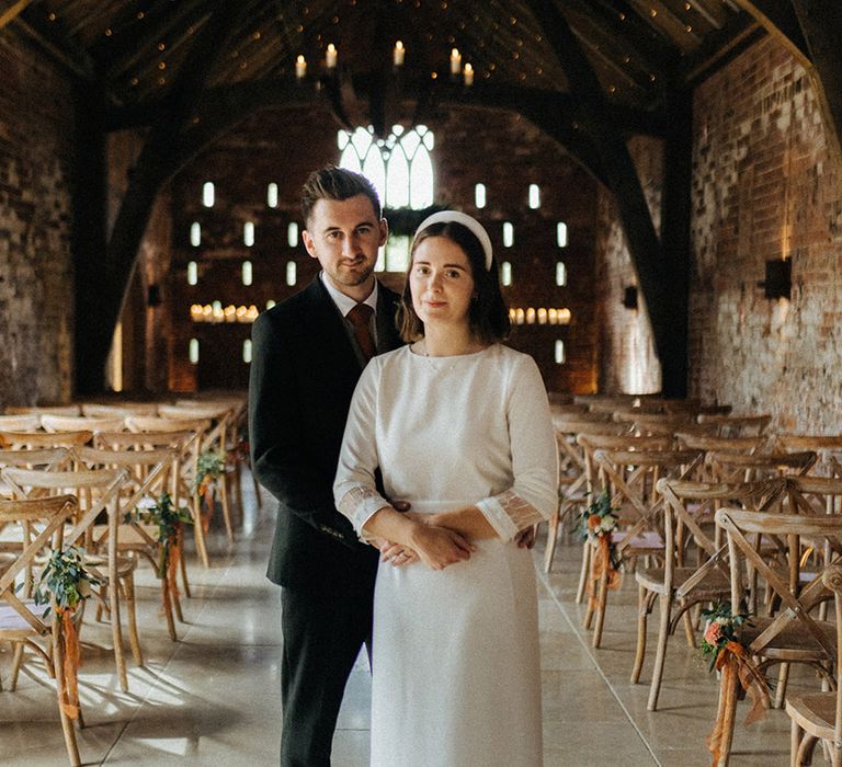 Groom in three piece suit with orange tie wearing tight coloured shoes embraces the bride from behind at Grangefields wedding venue 