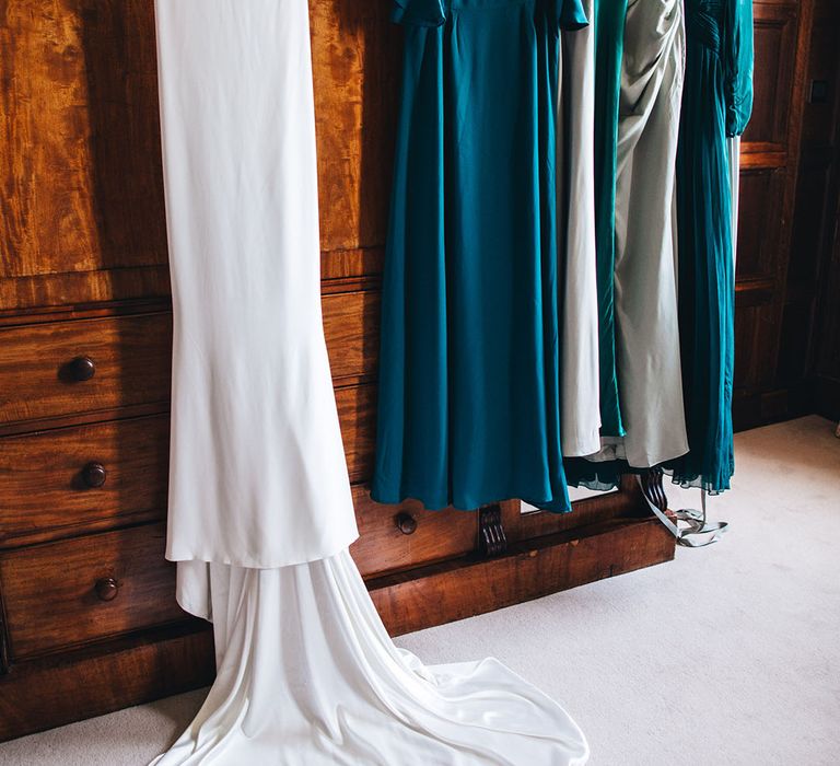 The bride's satin wedding dress hanging up with the bridesmaids dresses in different shades of green 