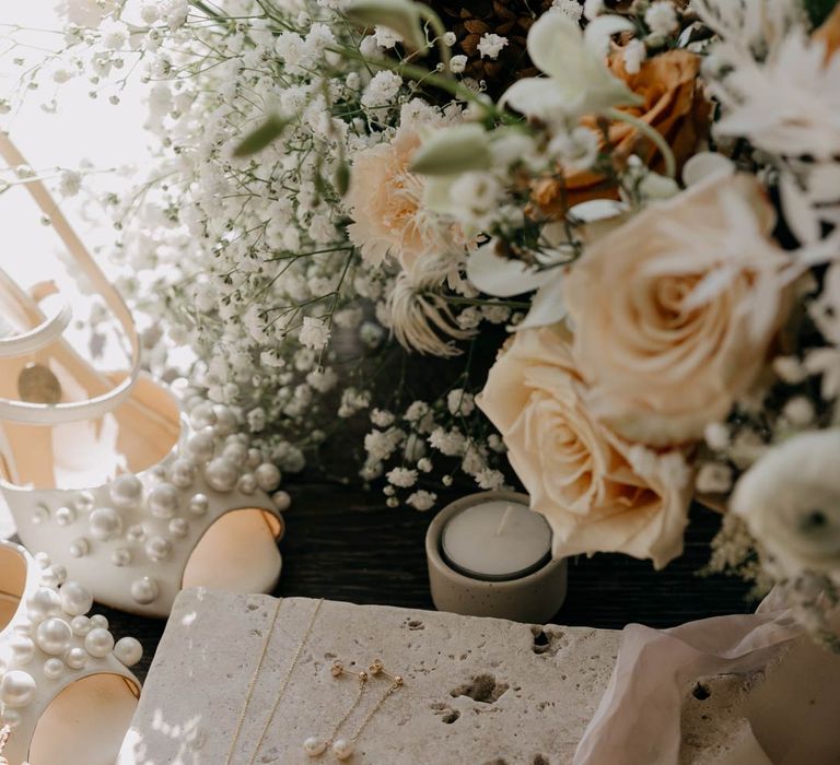 Pearl wedding necklace and earrings on large decorative stone slate surrounded by garden roses and baby's-breath flowers  