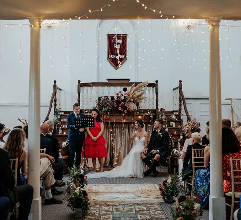 Wedding readings at bespoke boho wedding ceremony with world rugs, fairy lights and fabric banner decor 