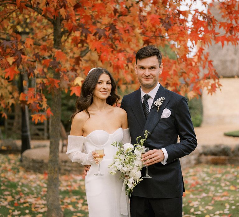 Groom in dark suit and tie dirking a glass of champagne with the bride in a strapless wedding dress with detachable sleeves and white wedding bouquet