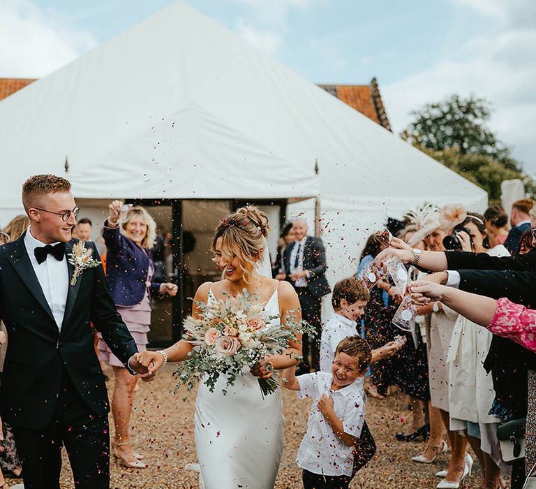 Groom in black tuxedo with dried flower buttonhole has confetti exit after the ceremony with the bride 