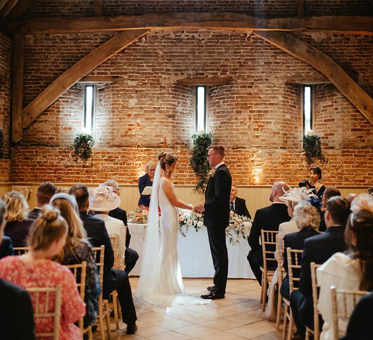 Elms Barn wedding venue in Suffolk with the bride and groom standing holding hands at the altar 