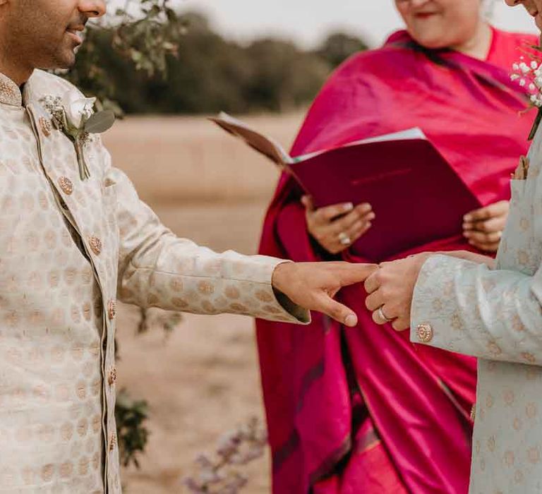 Groom in mint green Indian Sherwani holding hand of groom in cream and gold Indian sherwani with wedding celebrant in magenta lehenga 