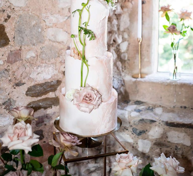 Fairytale wedding cake with four tiers, buttercream icing, and garden rose and stem decorations on brass cake stand at Pentney Abbey wedding 