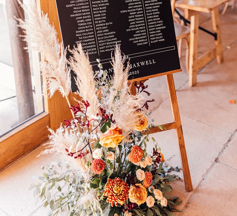 Black and white wedding table plan signage on wooden easel with autumnal flower arrangement with pampas grass for Old Gore Barn wedding 