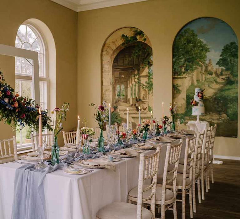 Classic wedding tablescape at Braxted Park wedding venue with white wedding tablecloth, cornflower blue wedding table runner, bright blue glass bottles with dried flowers, pastel tapered candles and spring floral arrangements 