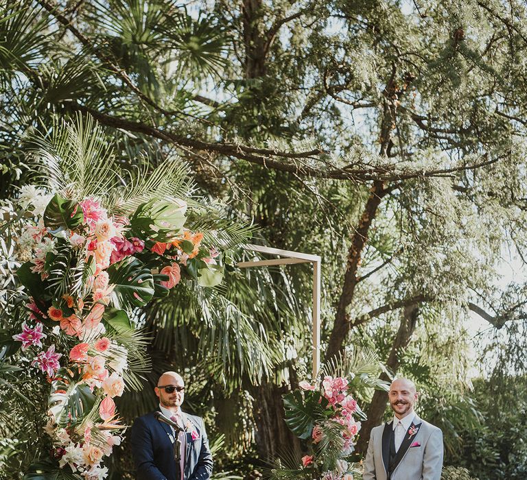 groom in a grey suit standing at outdoor wedding ceremony at Italian villa wedding venue with tropical flower arch