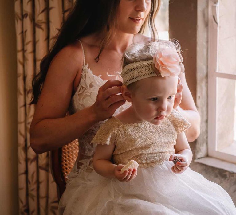 Bride in lace sleeveless wedding dress with puddle train helping her baby into her wedding outfit at Giraffe Manor wedding venue