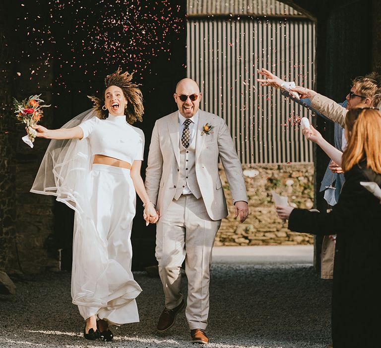 The bride and groom walk out of their ceremony beaming as guests throw confetti 