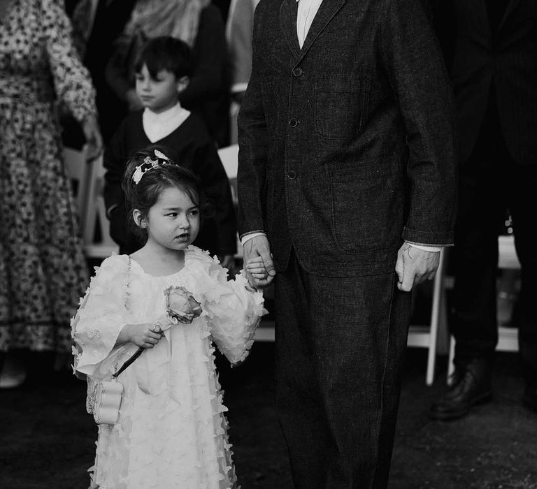 Groom standing with little flower girl in white butterfly dress 