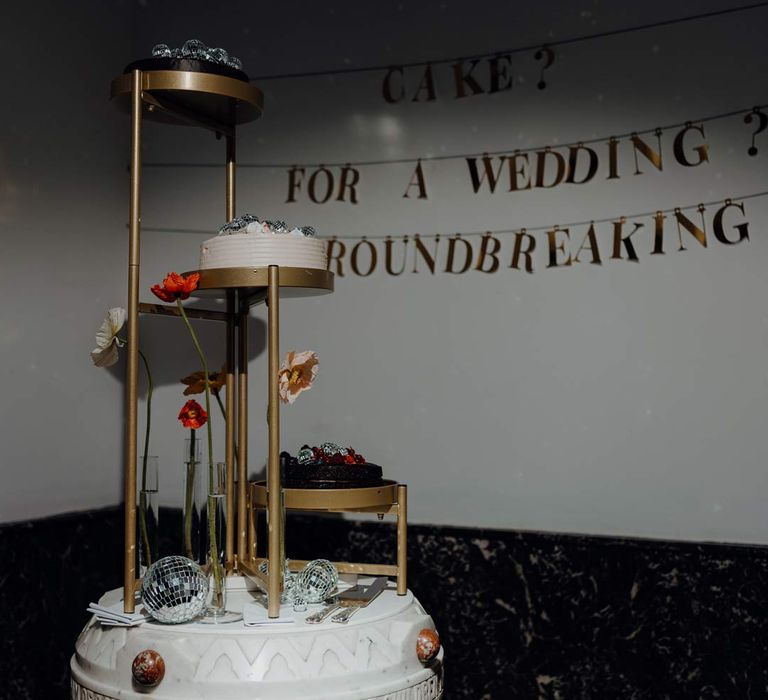 Three tiered golden wedding cake stands with three single tier wedding cakes with disco ball toppers and decor, single poppy flowers in test tube vases and golden funny wedding sign