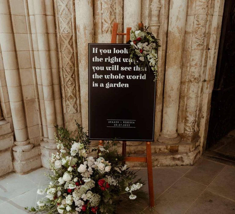 Monochrome wedding sign on wooden easel with large white garden rose, carnation and foliage flower arrangements 