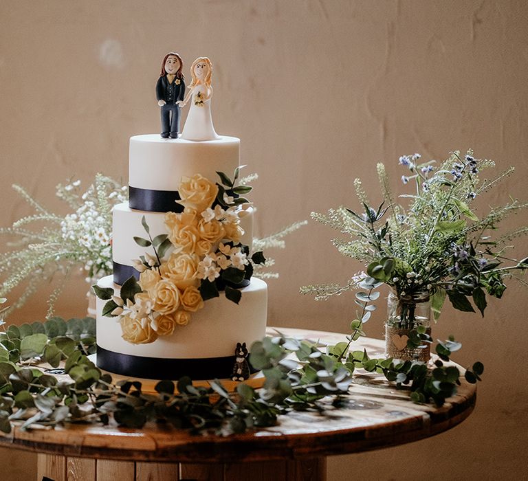 three-tier iced wedding cake with black ribbon and training flowers 