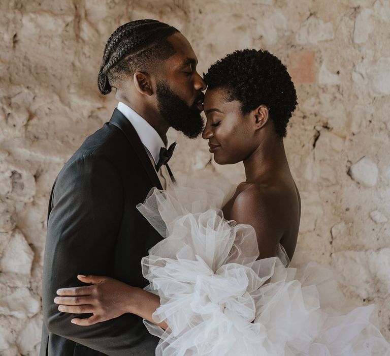 Bride in tulle wedding dress with off the shoulder detail kissing groom in black tux 