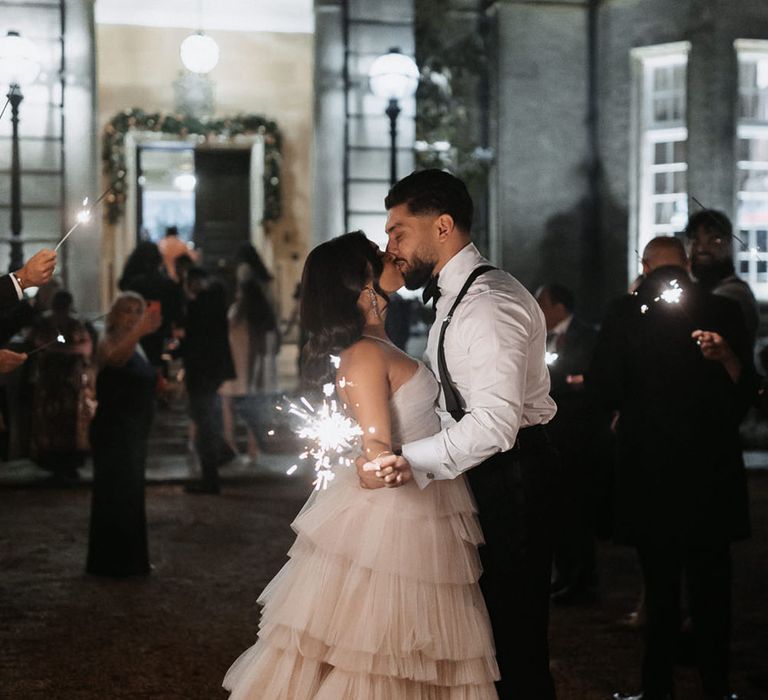 Bride wearing ruffle wedding reception dress by Alena Leena with groom in white shirt with black bow tie for sparkler send off 