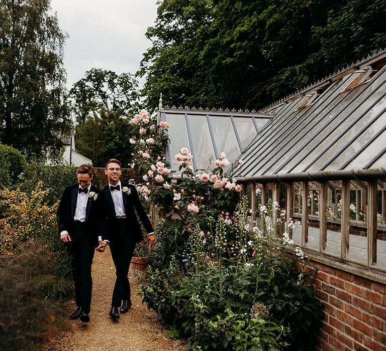 Two grooms in black tie walk around the gardens at their wedding venue 