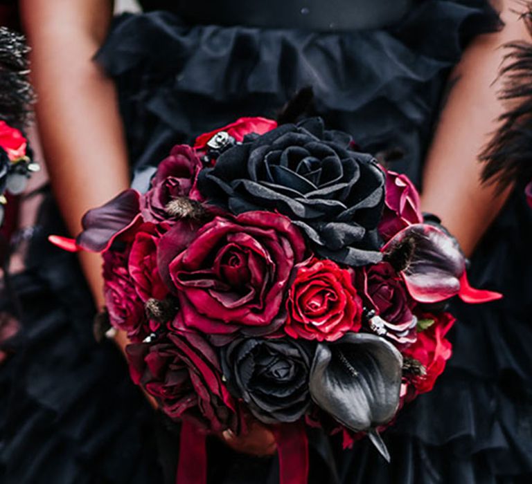 Bride holding red and black rose wedding bouquet with dyed lilies and more in round shape bouquet 