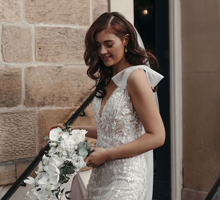 Bride holding a cascading white wedding bouquet in a fitted wedding dress with bow straps 