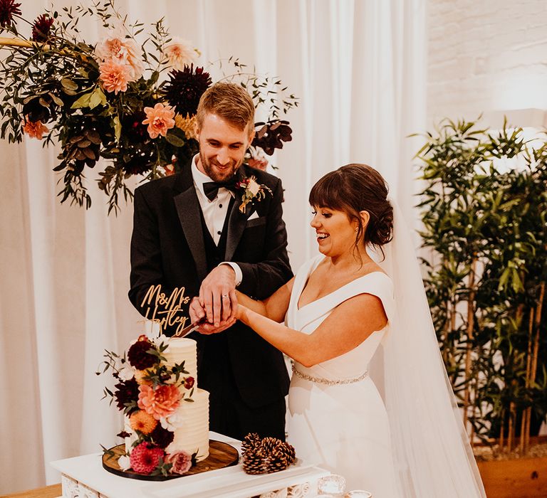 The bride and groom in traditional black tie wedding outfits cut their wedding cake 